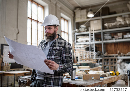 Mature male carpenter looking at blueprints plans in carpentery workshop. Small business concept. 83752237