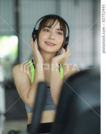 Fitness woman listening music via her wireless headphone while working out on treadmill. 83752445