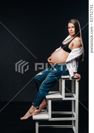 pregnant woman sitting on a ladder chair in a studio on a black background 83752741