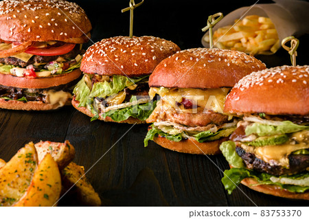 Assorted burgers with different fillings, with sesame seeds on wooden table isolated on black background. 83753370