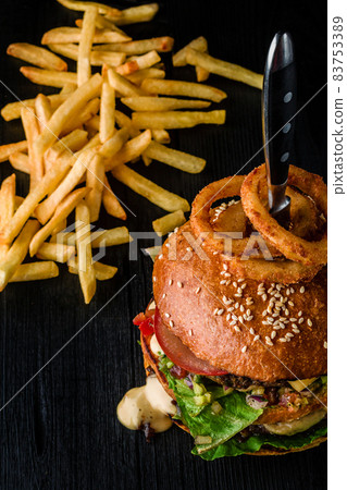Cheese burger with grilled meat, cheese, tomato and with onion rings on dark wooden surface. Ideal for advertisement. Close-up Cheese burger with grilled meat, cheese, tomato and with onion rings on dark wooden surface. Ideal for advertisement. Close-up 83753389