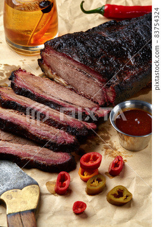 Fresh Brisket BBQ beef sliced for serving against a kraft paper background with sauce, hot peppers and corn. 83754324