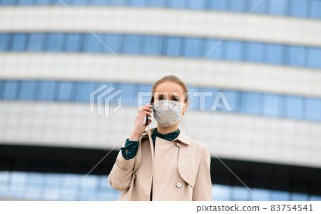 A young businesswoman wearing a health mask and talking on the phone in the city 83754541