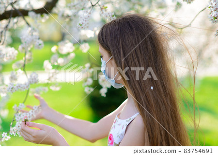 Lonely teenage girl wearing protection medicine mask against virus and allergy enjoying spring flower blossom in blooming garden 83754691