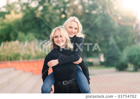 Two young females walking smiling embracing and kissing outdoor in the city 83754702