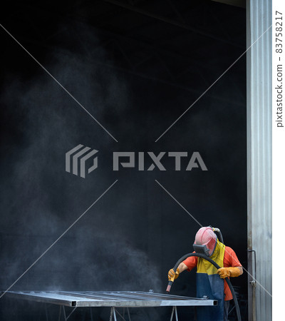 Operator of sandblasting machine polishing metal at workshop 83758217