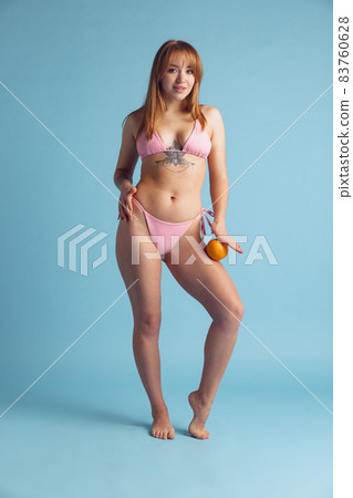 Portrait of young beautiful red-headed woman in inner wear posing isolated over blue studio background. Natural beauty concept. Portrait of young beautiful red-headed woman in inner wear posing isolated over blue studio background. Natural beauty concept. 83760628