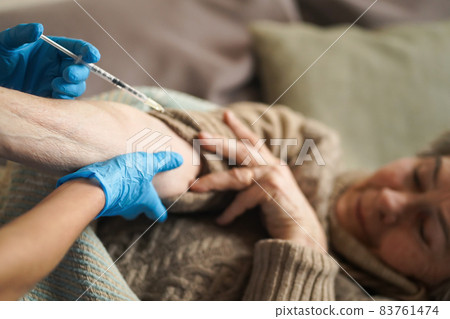 Nurse makes an injection with the vaccine to the patient at home. 83761474