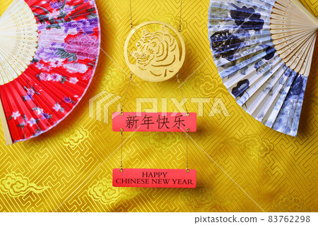 Gold tiger symbol and pair of chinese bamboo paper fans on yellow fabric with traditional chinese ornament with clouds. Chinese New Year of the Tiger 2022. Translation: happy new year 83762298