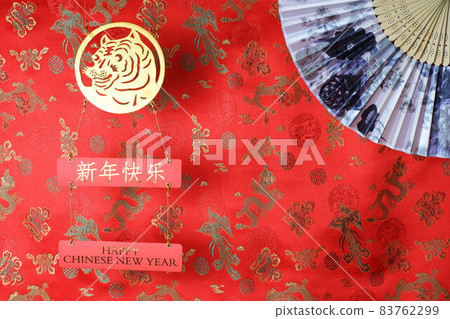 Golden tiger symbol and chinese bamboo paper fan on red fabric with traditional chinese ornament birds and dragons. Chinese New Year of the Tiger 2022. Translation: happy new year Golden tiger symbol and chinese bamboo paper fan on red fabric with traditional chinese ornament birds and dragons. Chinese New Year of the Tiger 2022. Translation: happy new year 83762299
