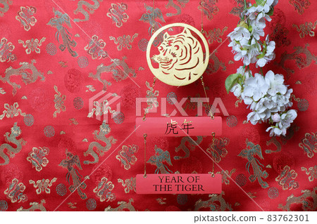 Golden tiger symbol and branch of white sakura cherry blossom on red fabric with traditional chinese ornament birds and dragons. Chinese New Year of the Tiger 2022. Translation: year of the tiger Golden tiger symbol and branch of white sakura cherry blossom on red fabric with traditional chinese ornament birds and dragons. Chinese New Year of the Tiger 2022. Translation: year of the tiger 83762301