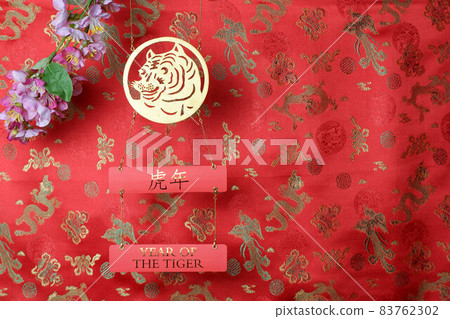 Golden tiger symbol and branch of pink sakura cherry blossom on red fabric with traditional chinese ornament birds and dragons. Chinese New Year of the Tiger 2022. Translation: year of the tiger 83762302