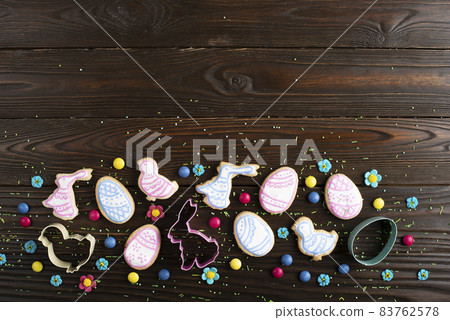 Cookie cutters and Easter frosted cookies in shape of egg, chicken and rabbit on dark wooden background. Flat lay with copy space. 83762578
