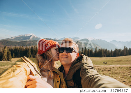 Couple making selfie photo high in the snow mountains enjoying the view. Freedom, happiness, travel and vacations concept, outdoor activities, she wearing in red hat and he a green jacket 83764887