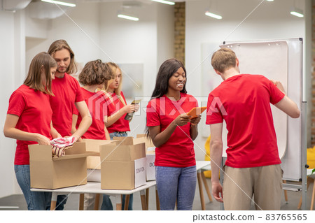 Young people in red looking busy while working with donations distributing Young people in red looking busy while working with donations distributing 83765565