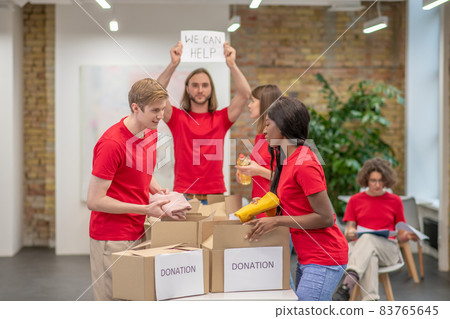 Young volunteers in red tshirts distributing donations in a sorting center Young volunteers in red tshirts distributing donations in a sorting center 83765645