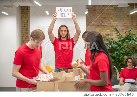 Young volunteers in red tshirts distributing donations in a sorting center 83765646