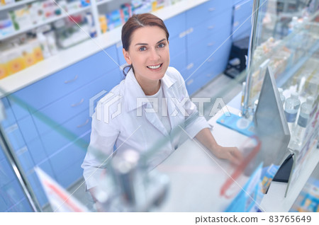 Woman in white coat near pharmacy cash register Woman in white coat near pharmacy cash register 83765649