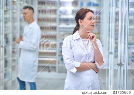 Pensive woman in uniform and employee at pharmacy Pensive woman in uniform and employee at pharmacy 83765669