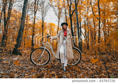 Young woman in classic trench coat with retro bicycle in yellow autumn park. Amazing scene of trendy 83765726
