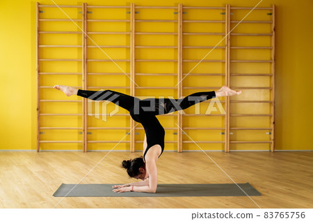 Woman indoors in retreat space doing handstand pose and legs in twine. Strong hands. Young lady in Woman indoors in retreat space doing handstand pose and legs in twine. Strong hands. Young lady in 83765756
