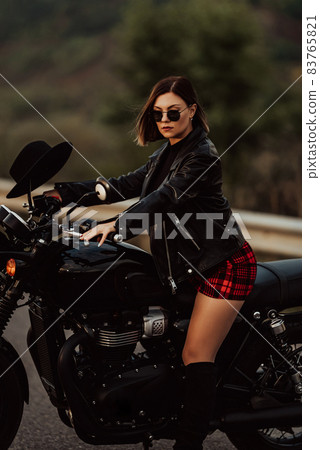 Portrait of stylish woman sitting on classic black retro-styled motorcycle while standing on road Portrait of stylish woman sitting on classic black retro-styled motorcycle while standing on road 83765821