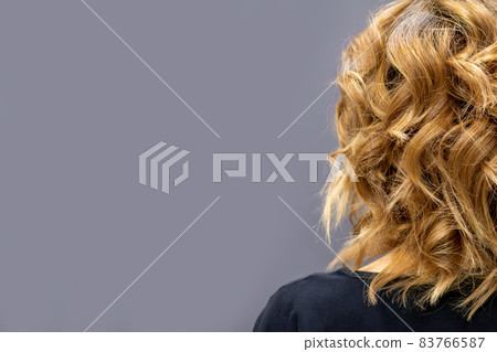 Back view of the woman with long brown curly hair stands on a dark background. Back view of the woman with long brown curly hair stands on a dark background. 83766587