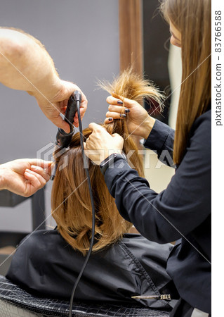The rear view of two hairdressers are curling hair for a young woman with electric hair iron in a beauty salon. The rear view of two hairdressers are curling hair for a young woman with electric hair iron in a beauty salon. 83766588