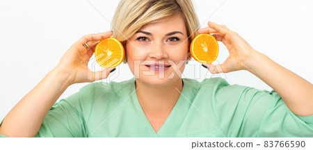 Portrait of young smiling blonde woman cosmetologist with halves of oranges on white background. Portrait of young smiling blonde woman cosmetologist with halves of oranges on white background. 83766590