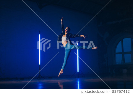 Young woman in casual style - jeans and leather jacket doing ballet in modern studio. Attractive Young woman in casual style - jeans and leather jacket doing ballet in modern studio. Attractive 83767412