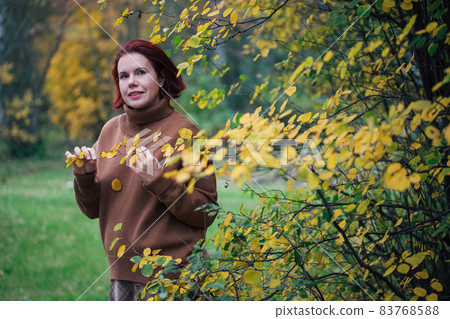 Portrait Of A Mature Woman against yellow forest trees in the autumn Portrait Of A Mature Woman against yellow forest trees in the autumn 83768588