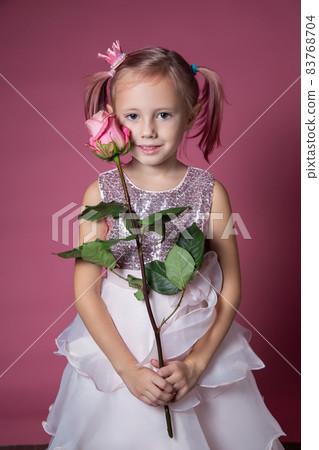 Little caucasian girl in a festive dress with sequins posing with rose flower Little caucasian girl in a festive dress with sequins posing with rose flower 83768704