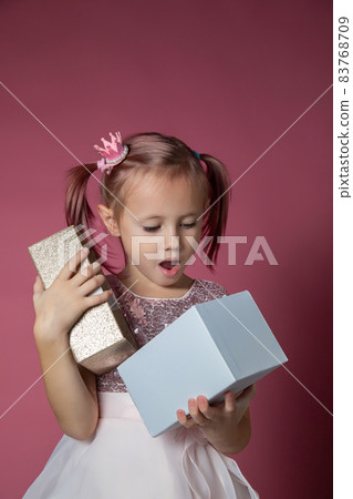 Little caucasian girl in a festive dress with sequins posing opening gift box 83768709