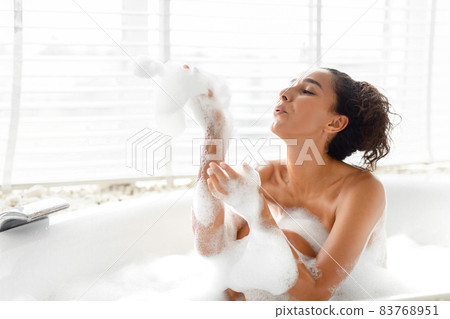 Beautiful young woman blowing soap bubbles and having fun in bath at home, copy space Beautiful young woman blowing soap bubbles and having fun in bath at home, copy space 83768951