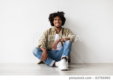Portrait Of Smiling Handsome Black Guy Relaxing On Floor Near White Wall Portrait Of Smiling Handsome Black Guy Relaxing On Floor Near White Wall 83768960