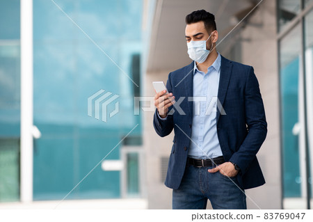 Middle eastern entrepreneur in face mask using phone while walking Middle eastern entrepreneur in face mask using phone while walking 83769047