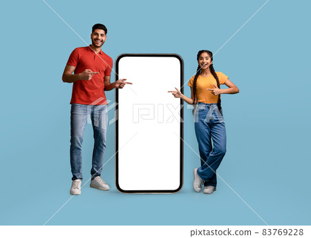 Mobile Offer. Cheerful Arab Couple Pointing At Big Cellphone With White Screen Mobile Offer. Cheerful Arab Couple Pointing At Big Cellphone With White Screen 83769228