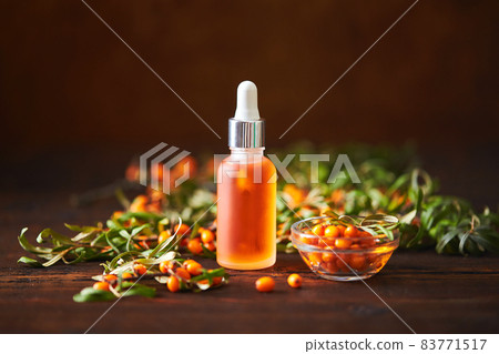 Glass bottle with sea buckthorn oil berries and sea buckthorn branches on wooden background 83771517