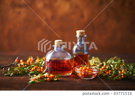 Glass bottle with sea buckthorn oil berries and sea buckthorn branches on wooden background 83771518