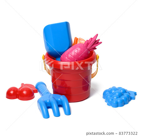 baby red plastic bucket with shovel and toys isolated on white background. Outdoor items 83773322