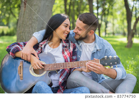 Handsome man teaching girl to play guitar. Guitar teacher. romantic date in nature with a guitar. Perfect first date Handsome man teaching girl to play guitar. Guitar teacher. romantic date in nature with a guitar. Perfect first date 83774750