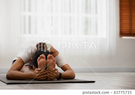 In the morning, an Asian woman is doing yoga,sitting forward bend exercise, head to knees, uttanasana stance, working out, and wearing sportswear. In the morning, an Asian woman is doing yoga,sitting forward bend exercise, head to knees, uttanasana stance, working out, and wearing sportswear. 83775735