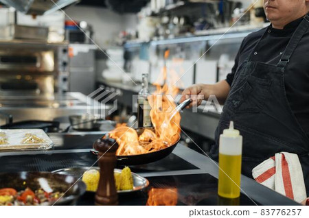 side view male chef flambeing dish. High quality beautiful photo concept side view male chef flambeing dish. High quality beautiful photo concept 83776257