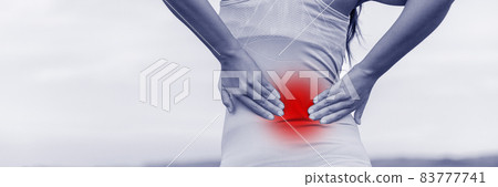 Back pain - woman having painful muscle injury in lower back. Fitness girl sport girl with sports injury outdoor. Blue filter with red zone circle showing the painful area. Back pain - woman having painful muscle injury in lower back. Fitness girl sport girl with sports injury outdoor. Blue filter with red zone circle showing the painful area. 83777741