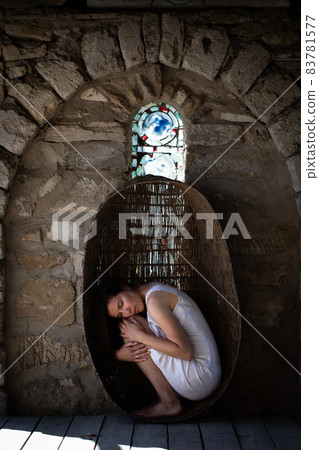 A woman sits in a large wicker basket, hugging her knees. The concept of motherhood, self-knowledge, awareness. A woman sits in a large wicker basket, hugging her knees. The concept of motherhood, self-knowledge, awareness. 83781577
