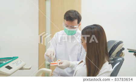 A caucasian dentist man, people showing how to use dental floss with typodont teeth model to Asian patient at hospital clinic. Cleaning. Doctor. Dentistry, medical and health. A caucasian dentist man, people showing how to use dental floss with typodont teeth model to Asian patient at hospital clinic. Cleaning. Doctor. Dentistry, medical and health. 83783654