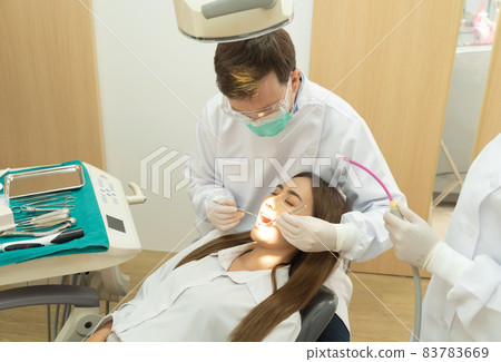 A dentist checking up Asian woman patient's teeth by using dental mouth mirror at hospital clinic. Teeth check up with dental tools. Doctor. Dentistry, medical and health. People. 83783669