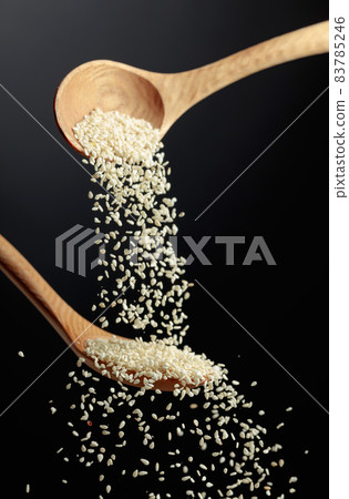 Grains of sesame are poured with wooden spoons. 83785246