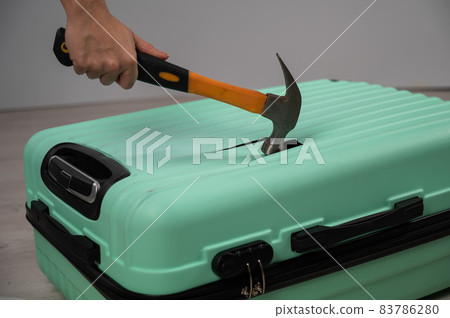 A woman hits a suitcase with a hammer on a white background. 83786280