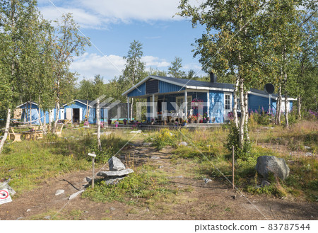 Beautiful blue sami or saami country house at Sitojaure lake shore with birch trees and flower pots. At Kungsleden hiking trail, Sweden Lapland. Summer sunny day, blue sky, white clouds Beautiful blue sami or saami country house at Sitojaure lake shore with birch trees and flower pots. At Kungsleden hiking trail, Sweden Lapland. Summer sunny day, blue sky, white clouds 83787544